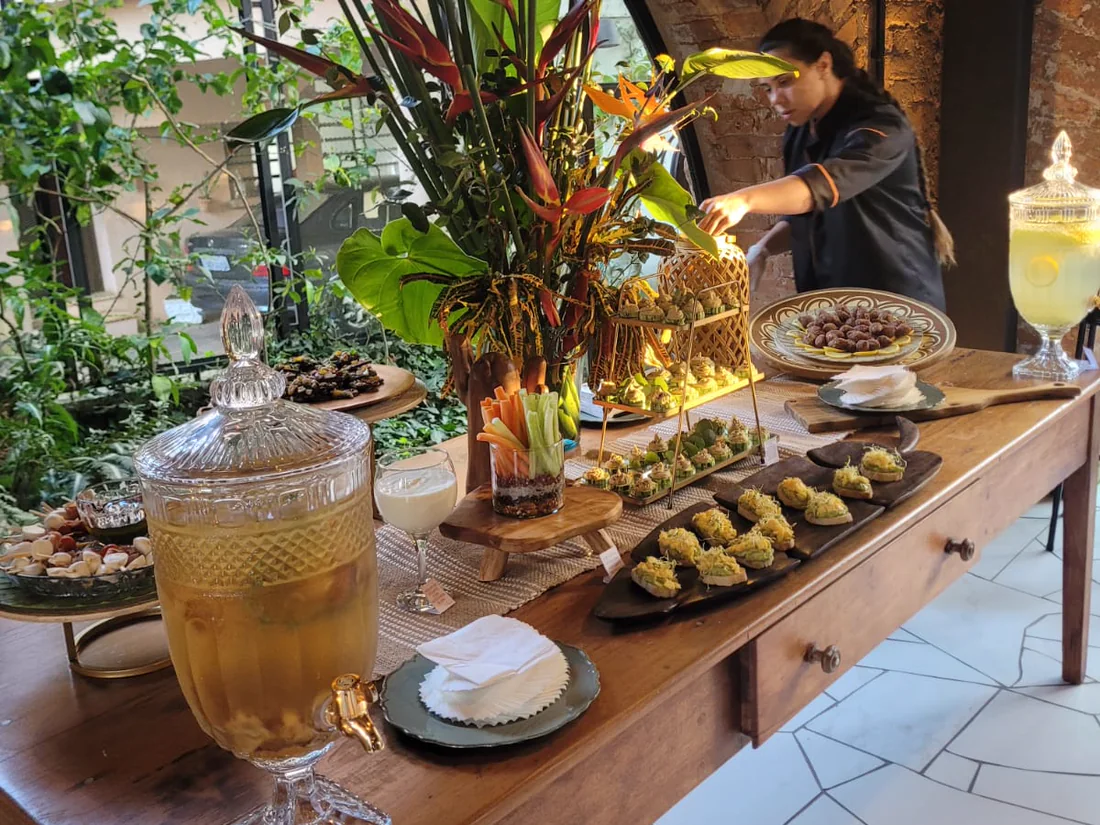 Mesa de buffet montada com finger foods, flores tropicais e bebidas